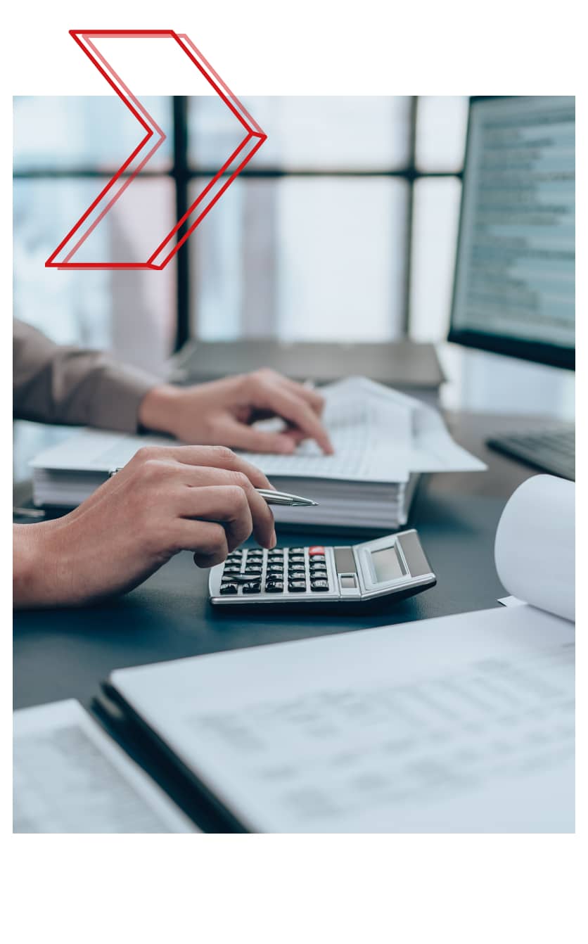Close-up of a person using a calculator and reviewing financial documents at a desk, with a computer screen in the background—illustrating Fexco’s support for global payments in lesser-traded currencies.