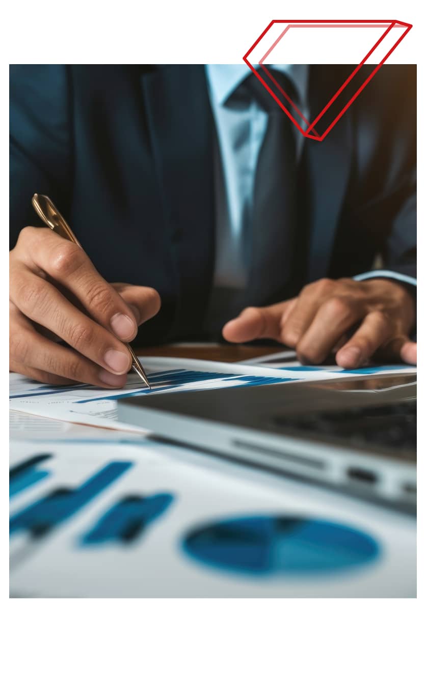 Close-up of a business professional in a suit analysing charts and graphs with a pen at a desk, next to a laptop - representing Fexco's currency risk management solutions for SMEs.