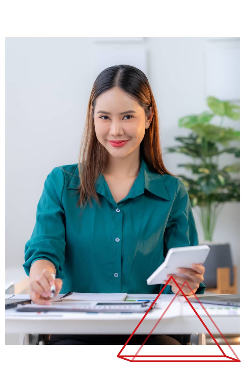 Smiling woman in a green blouse working at a desk with a smartphone and tablet, representing Fexco’s competitive FX rates and low-fee international payment solutions